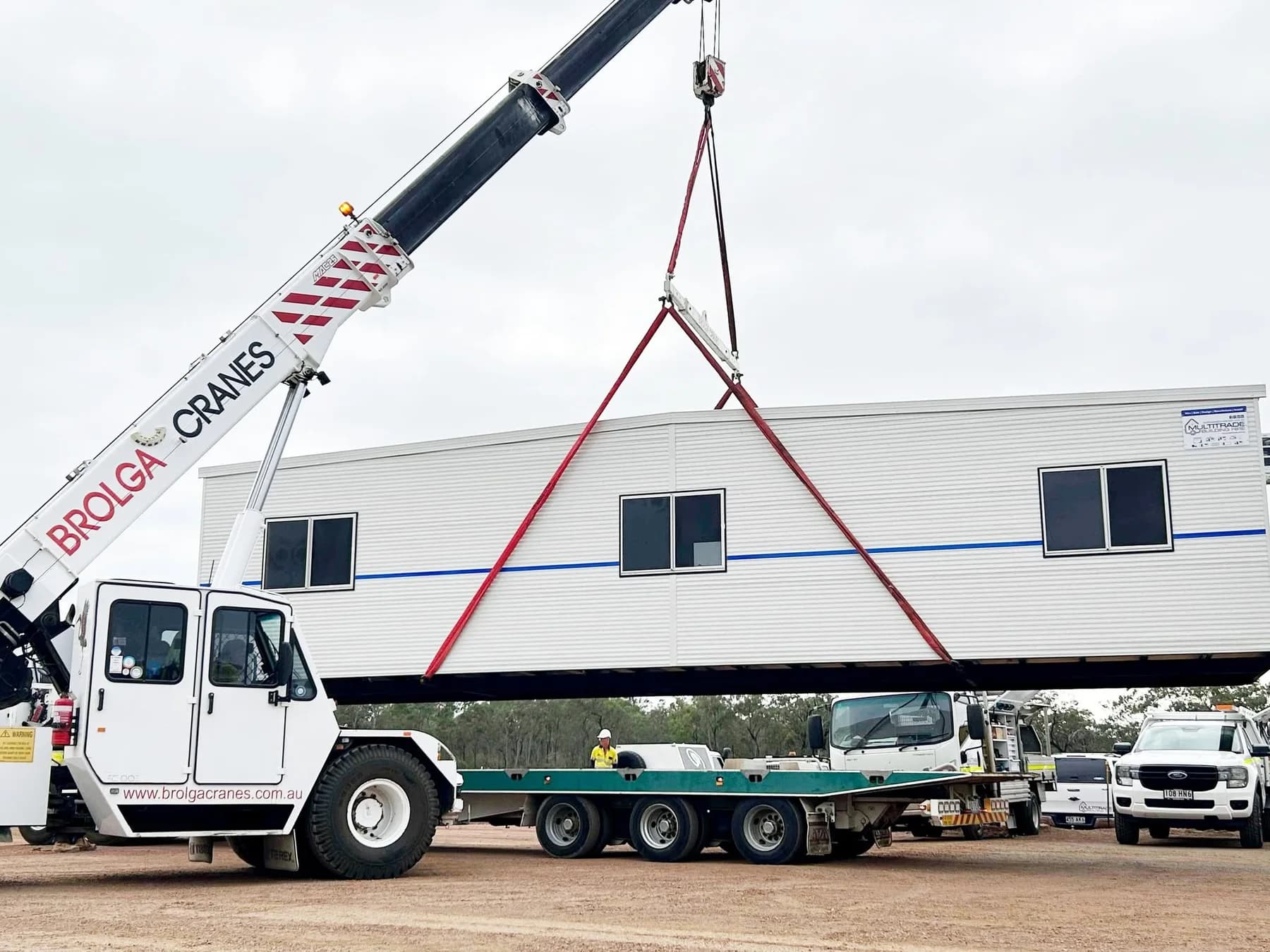Portable building suspended above a transport trailer during crane placement